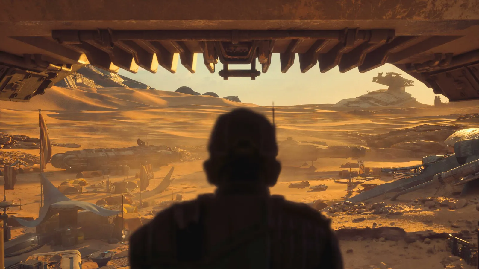 Silhouette of a helmeted figure seen from behind, looking out from under a large hangar overhang at a desert settlement dotted with parked ships